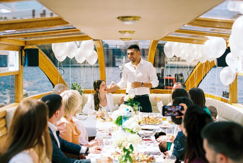 A man standing at the top of a table with people.