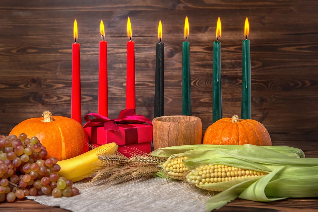 Kwanzaa festival concept with seven candles red, black and green, gift box, pumpkins, ears of wheat, grapes, corns, banana, bowl and fruits on wooden background, close up (Kwanzaa festival concept with seven candles red, black and green, gift box, pum